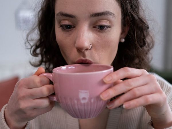 Person calmly sipping tea and looking out a window, embodying mindfulness.
